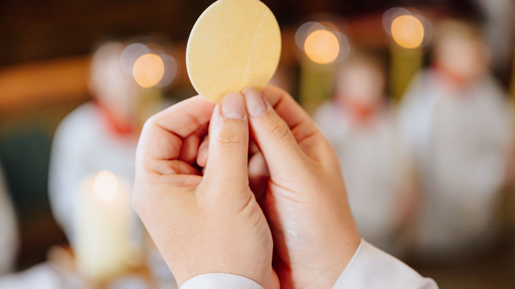 Symbolbild für die Erstkommunion. Ein Pfarrer hällt die Hostie hoch. 